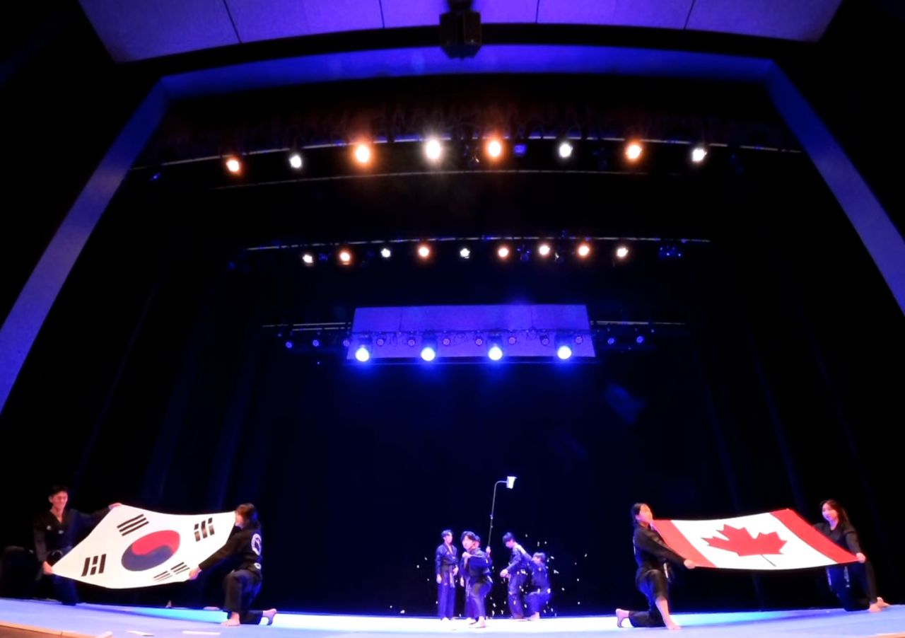 Rim’s Taekwondo 시범단이 무대 중앙에서 한국(태극기)과 캐나다(단풍잎) 국기를 들고 있는 모습. 태권도를 통한 양국 간의 문화 교류를 상징적으로 보여준다.